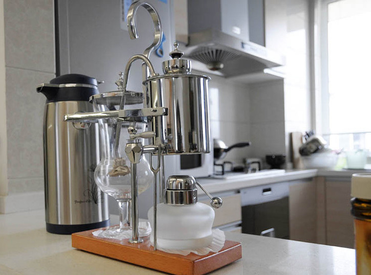 透过精致的咖啡机看厨房，也是一样的现代风，米灰色调。