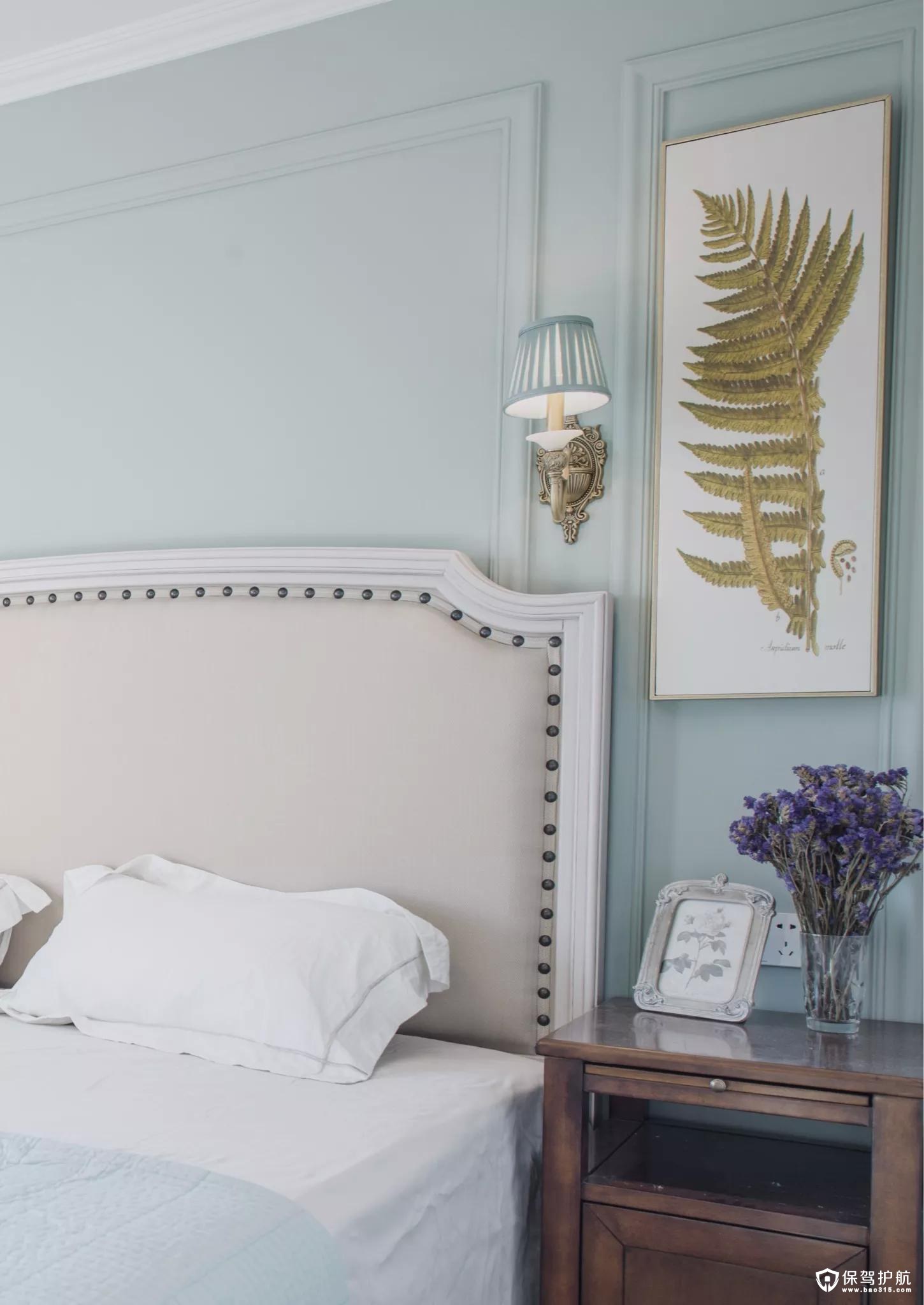 卧室的美式布衣床头靠垫，在清新的淡蓝色背景墙+线条边框，还有一旁的蕨类装饰画的衬托，整体给人以优雅温馨的气息。